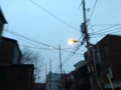 the street light is shining brightly in the foggy sky above some buildings and power lines