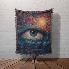 a tapestry with an eye on it hanging in front of a white brick wall and wooden floor