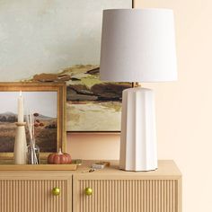 a white lamp sitting on top of a dresser next to a painting and a framed picture