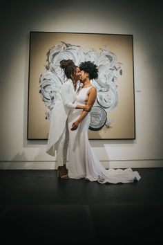 two people standing next to each other in front of a painting