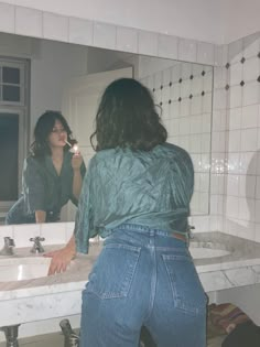 a woman standing in front of a bathroom mirror brushing her teeth