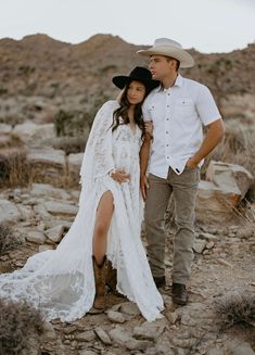 a man and woman in cowboy hats standing on rocks with their arms around each other