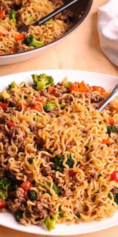 two white plates filled with noodles and broccoli on top of a wooden table