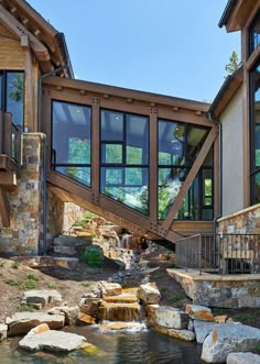 a house that has a waterfall in front of it and lots of windows on the side