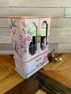 a cabinet with pink flowers painted on the front and sides, sitting on a wooden floor