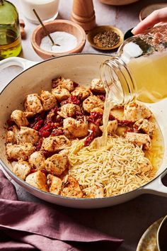 someone pouring sauce into a pan filled with pasta and tofu pieces, next to other ingredients