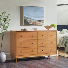 a bedroom with a bed, dresser and painting on the wall next to a potted plant