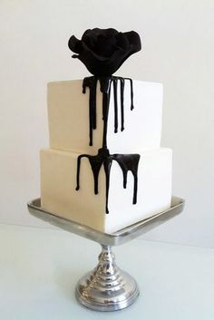 three tiered cake with white and black icing on the top, sitting on a silver platter