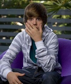 a young man sitting on a purple chair covering his mouth