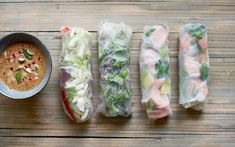 four different types of food wrapped in paper on a table next to a bowl of dipping sauce