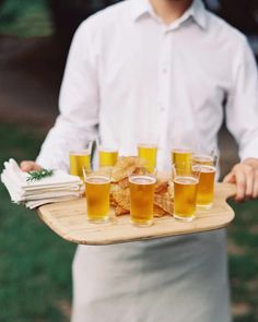 a man holding a tray with glasses of beer on it and napkins in front of him