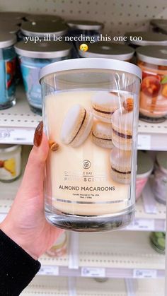 a person holding up a glass jar filled with cookies and almonds in front of shelves