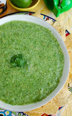 a white bowl filled with green salsa next to limes