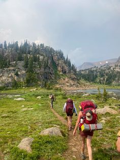 three people with backpacks are walking up a trail in the mountains near a lake