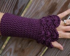 a woman's hand wearing purple knitted arm warmers on top of a wooden fence