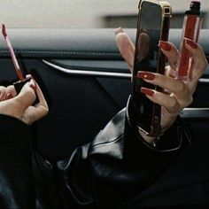 a woman holding up two cell phones in her hand while sitting in the back seat of a car