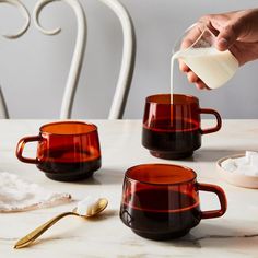 a person pouring milk into three coffee mugs