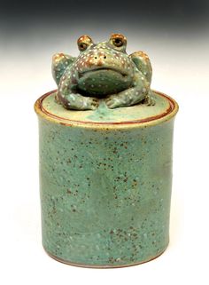 a ceramic frog sitting on top of a green container