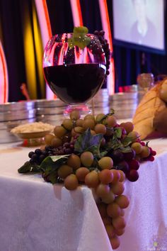 a glass of red wine and some grapes on a white table cloth with other items in the background