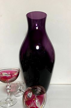 a purple vase sitting next to two wine glasses