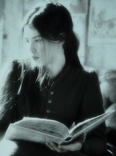 a woman sitting down reading a book with her hair blowing in the wind and looking off into the distance