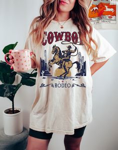 Embrace the spirit of the Wild West with our Vintage Western Cowboy Graphic T-Shirt. Perfect for those who love the rugged charm of cowboy culture and retro fashion, this shirt is a must-have for any wardrobe. Features: Vintage Design: A throwback to the 90s with a classic Western graphic that captures the essence of cowboy life. High-Quality Print: Durable and vibrant printing ensures the design stays bright and clear through many wears and washes. Comfortable Fit: Made from soft, breathable fa Trendy Short Sleeve T-shirt For Rodeo, Trendy Short Sleeve Rodeo T-shirt, Retro Graphic Print Tops For Rodeo, Retro Screen Print Tops For Rodeo, White Crew Neck T-shirt For Rodeo, Graphic Print Crew Neck T-shirt For Rodeo, White Graphic Tee For Rodeo, White Short Sleeve T-shirt For Rodeo, Retro Letter Print Tops For Rodeo