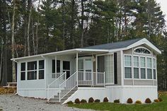 a mobile home sits in the middle of a wooded area with white railings and windows