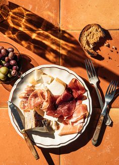 a white plate topped with meats and cheese next to a bowl of olives