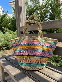 a multicolored straw bag sitting on top of a wooden bench next to trees