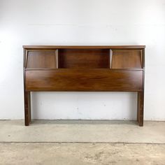 a wooden headboard sitting on top of a cement floor next to a white wall