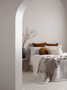 a bed with white sheets and brown pillows in a bedroom next to an arch shaped wall