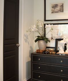 a black dresser with white flowers on top and a framed photograph above the drawers in front of it