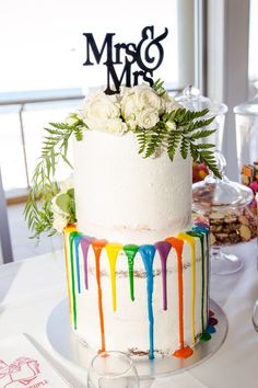 a wedding cake decorated with white roses and rainbow drips is sitting on a table