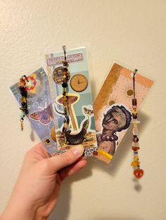 a person holding up some cards with charms attached to them and a clock hanging on the wall