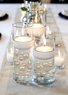 candles are lit on a long table with glass vases filled with water and pearls