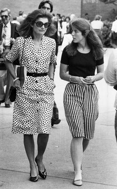 two women are walking down the street in black and white polka dot dresses, one is carrying a purse