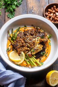 a white bowl filled with chicken and asparagus on top of a wooden table