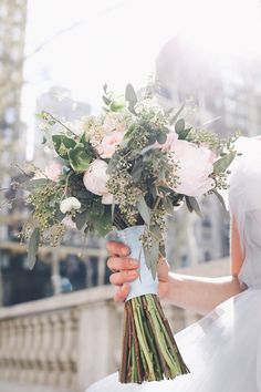 a bride holding a bouquet of flowers in her hand while standing on a bridge over looking the city