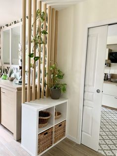 a white shelf with baskets and plants on it next to a kitchen counter in front of a mirror