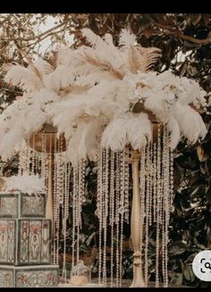 an arrangement of white feathers and beads hanging from a tall wooden pole in front of a tree