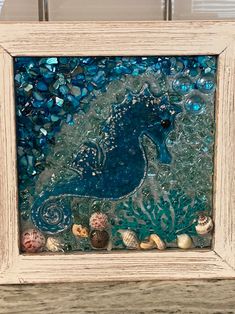 a blue sea horse surrounded by seashells in a white frame on a table