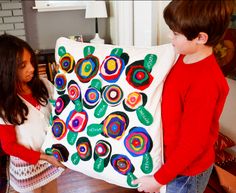 two children holding up a large pillow with colorful circles on it