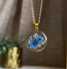 a glass necklace with blue flowers in it on a table next to a potted plant