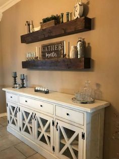 a white buffet table with two shelves above it and candles on the wall behind it