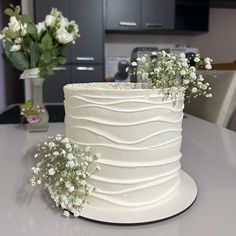 a white frosted cake sitting on top of a table next to a vase with flowers