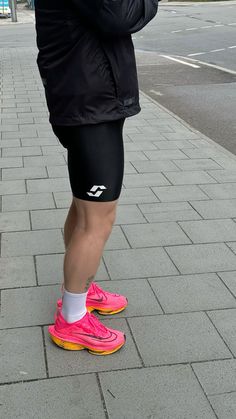 a person standing on the sidewalk with their legs crossed wearing running shorts and pink shoes