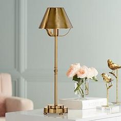 a white table topped with a vase filled with pink flowers next to a gold lamp