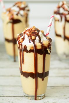 two glasses filled with ice cream and caramel on top of a white wooden table