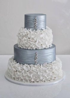 a three tiered wedding cake with white flowers on the bottom and silver ribbon around the top