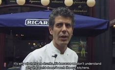 a man standing in front of a restaurant talking to someone on the street while wearing a chef's uniform